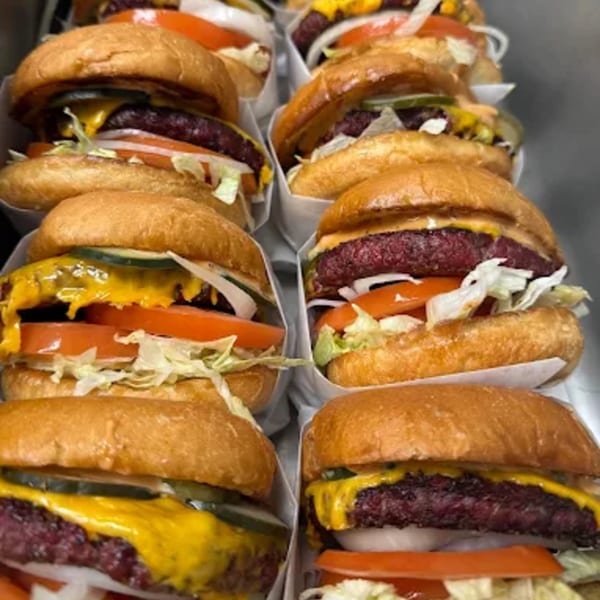 Rows of Hattie's BBQ cheeseburgers with lettuce, tomato, onion, and pickles in paper wrappers.