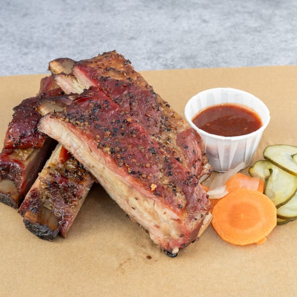 Hattie's BBQ ribs, with a side of sauce, pickles, and carrots on a brown paper.