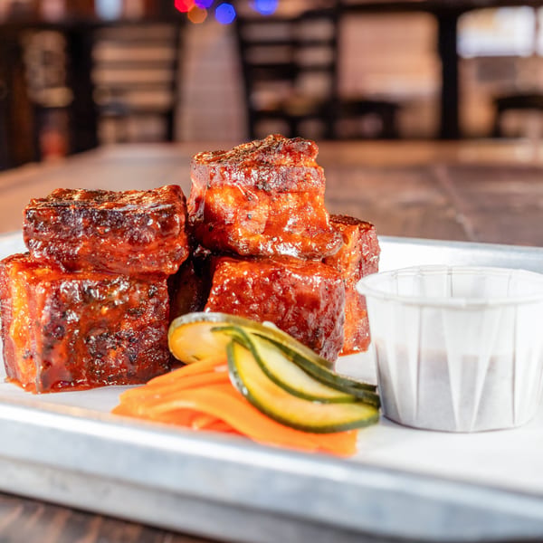 Hattie's BBQ burnt ends, glazed in sauce, with pickled carrots and cucumbers on a tray.