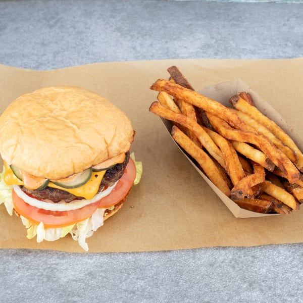 Hattie's BBQ cheeseburger with lettuce, tomato, onion, pickles, and fries on brown paper.