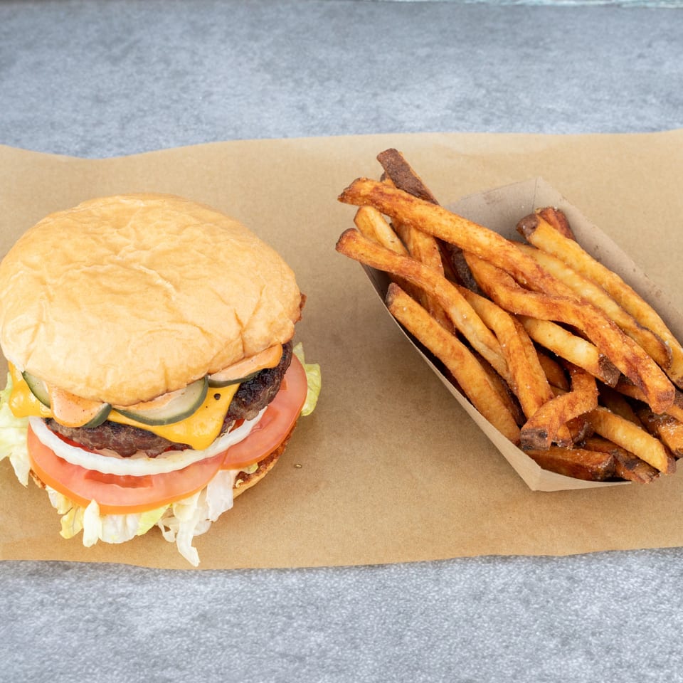 Hattie's BBQ cheeseburger with lettuce, tomato, onion, pickles, and fries on brown paper.